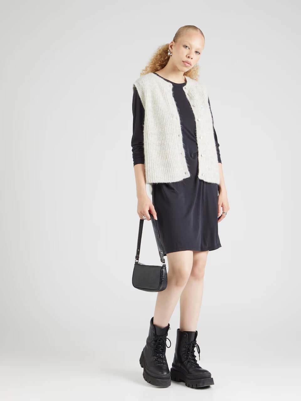 Model wearing Pieces Pcanora Short Dress with a knitted vest, paired with chunky black boots, showcasing women's fashion.