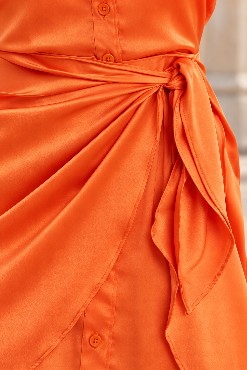 Close-up of the orange satin fabric, front buttons and wrap tie at the waist of the Guess shirt dress.