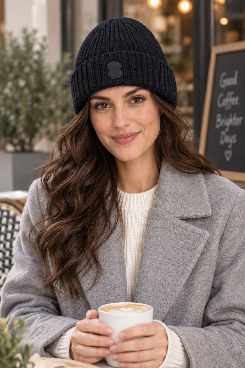 Woman wearing the s.Oliver navy beanie and a grey coat at an outdoor cafe