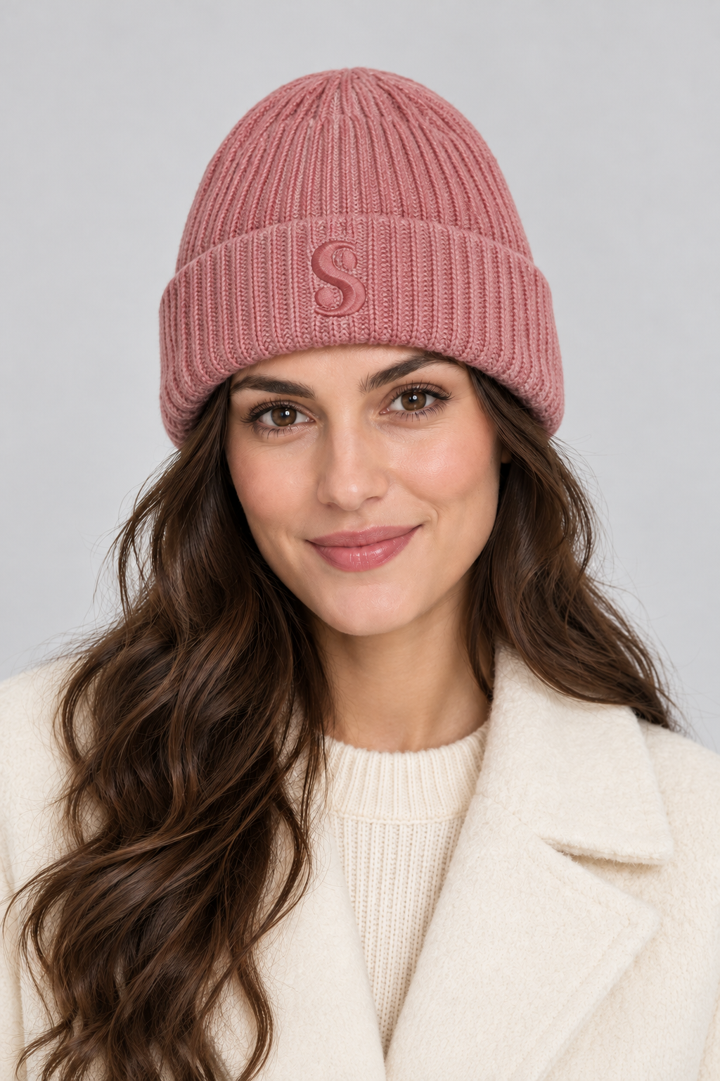 Woman wearing a dusty pink s.Oliver beanie with a folded cuff and embroidered S against a light studio background.