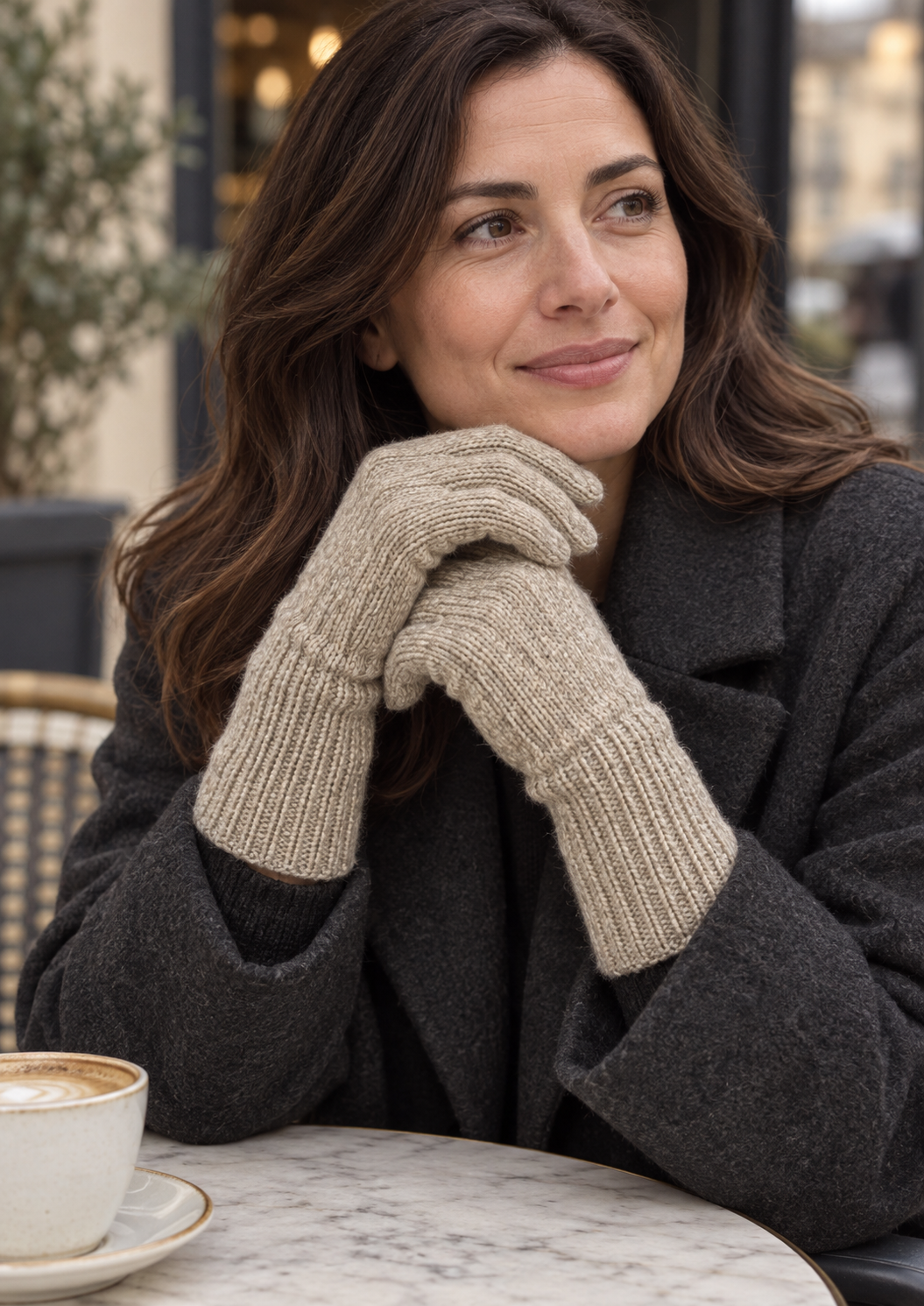 Model wearing beige s.Oliver knitted gloves with a charcoal coat at an outdoor café