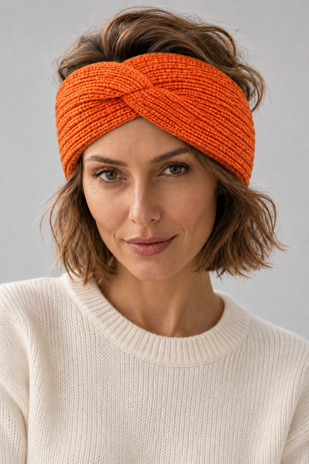 Woman wearing an orange s.Oliver knitted twist headband with a cream jumper against a neutral background
